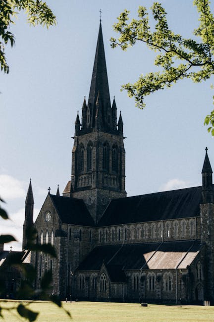 A black and white photograph of St. Mel's Cathedral showing its historic stone facade, tall arched entrance, and multiple spires, situated on a paved area with a short railing in front. Surrounding th